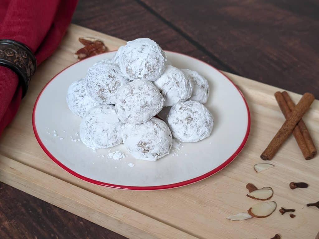 Spiced Cookie Balls on a plate on a tray next to cinnamon sticks, cloves, and shaved almonds - close up