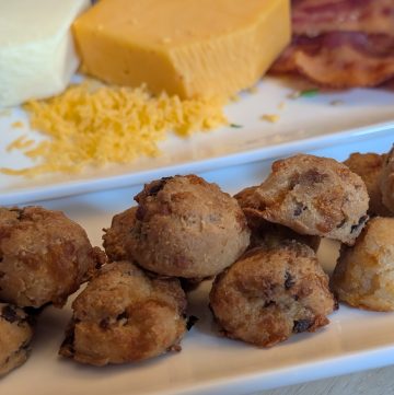 Cheesy Bacon Biscuit Bites - Plated with sliced of cooked bacon, a block of shredded cheddar cheese, and a block of shredded mozzarella cheese - Close up