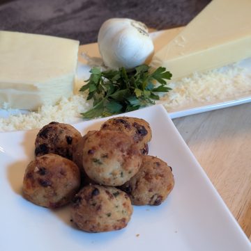 Cheesy Garlic Biscuit Bites - Plated with a block of shredded parmesan cheese, a block of shredded mozzarella cheese, a head of garlic, and fresh parsley - Close up