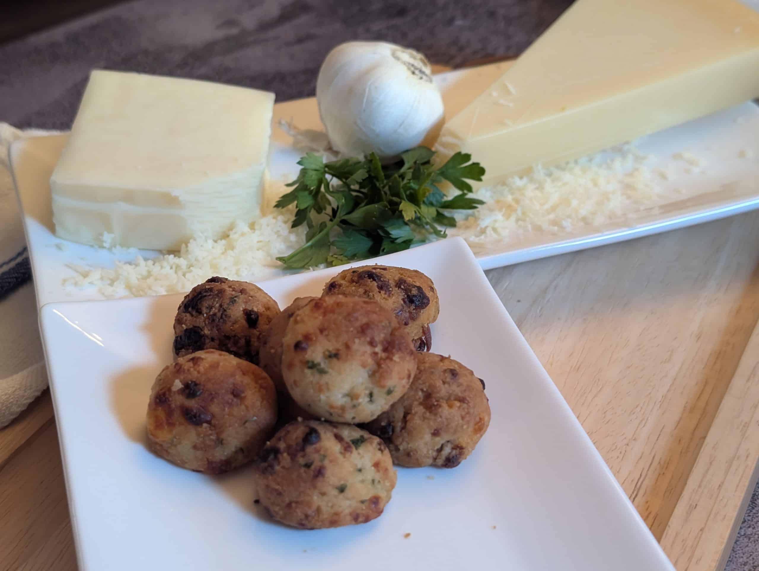 Cheesy Garlic Biscuit Bites - Plated with a block of shredded parmesan cheese, a block of shredded mozzarella cheese, a head of garlic, and fresh parsley - Close up